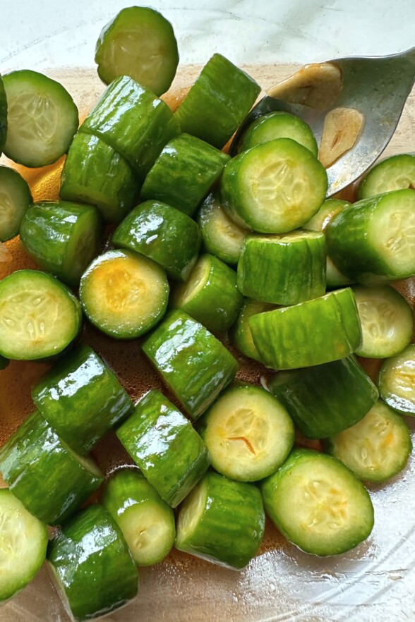 Sliced cucumbers tossed in a flavorful garlic-chili oil dressing in a mixing bowl
