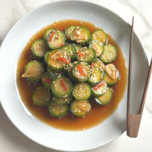 Spicy cucumber salad served in a white bowl with chili oil drizzle and garlic slices.