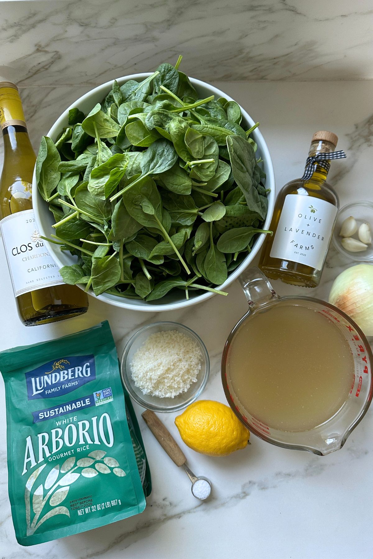 ingredients to make risotto on a counter, chicken broth parmesan, spinach, lemon juice, and olive oil