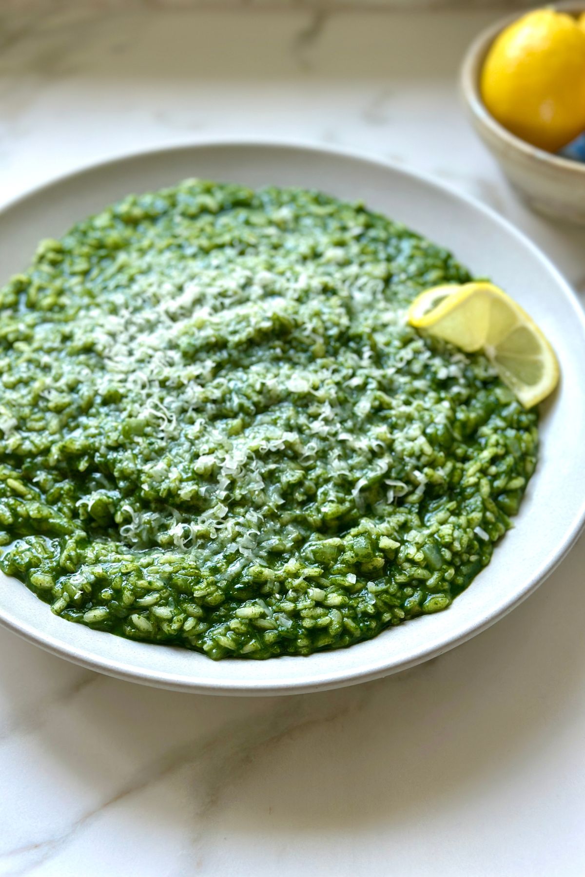 creamy spinach risotto in a white bowl with a lemon wedge