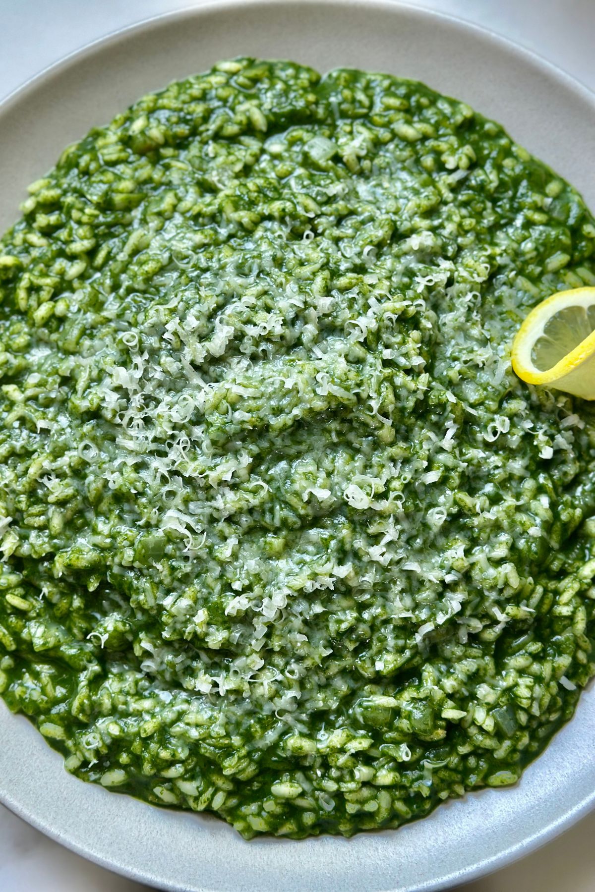 a close up of spinach risotto to show the small cooked arborio rice, spinach sauce, and parmesan cheese on top