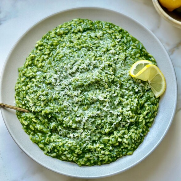 creamy spinach risotto topped with parmesan cheese and a lemon wedge.