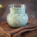 Small bowl of creamy Parmesan ranch dressing with flecks of fresh herbs on a tablecloth