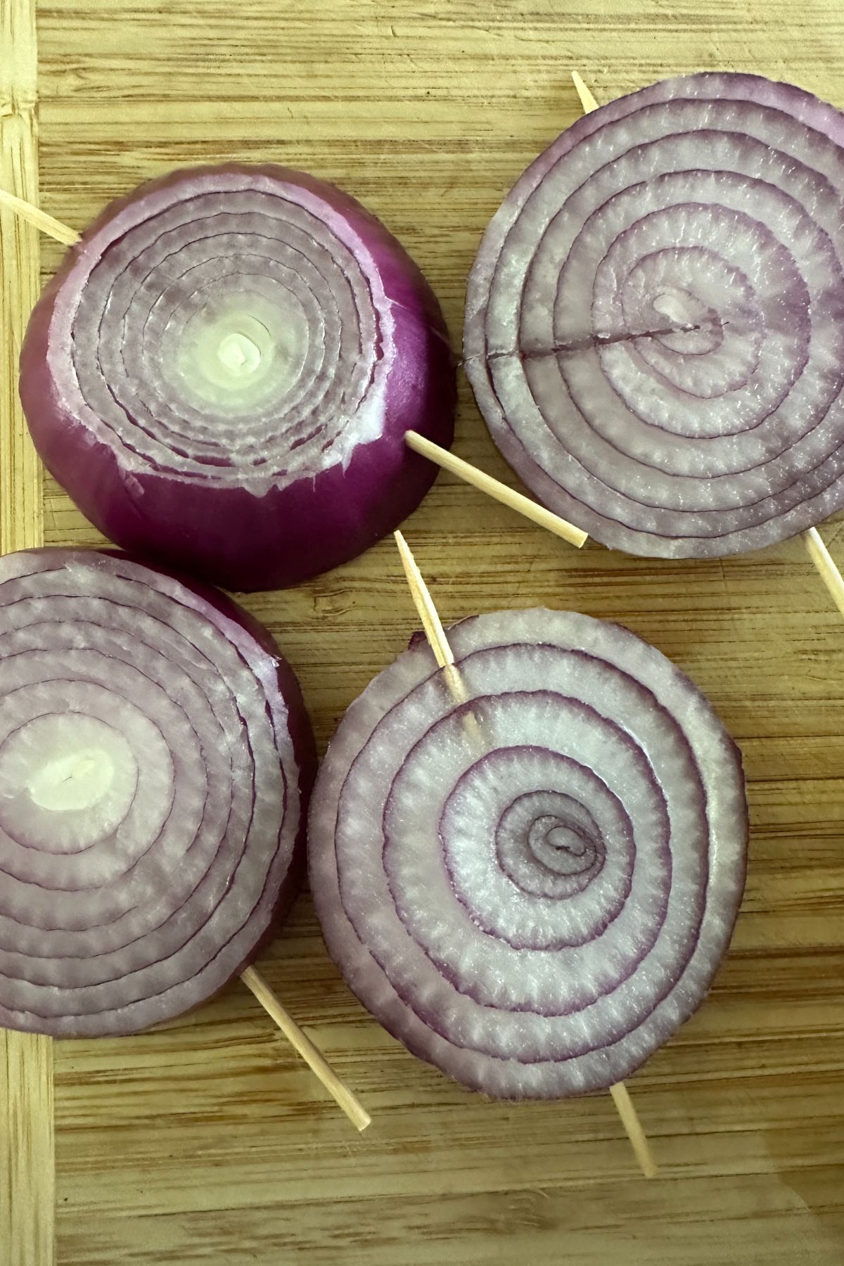 Red onion slices secured with toothpicks and brushed with marinade, prepped for grilling.
