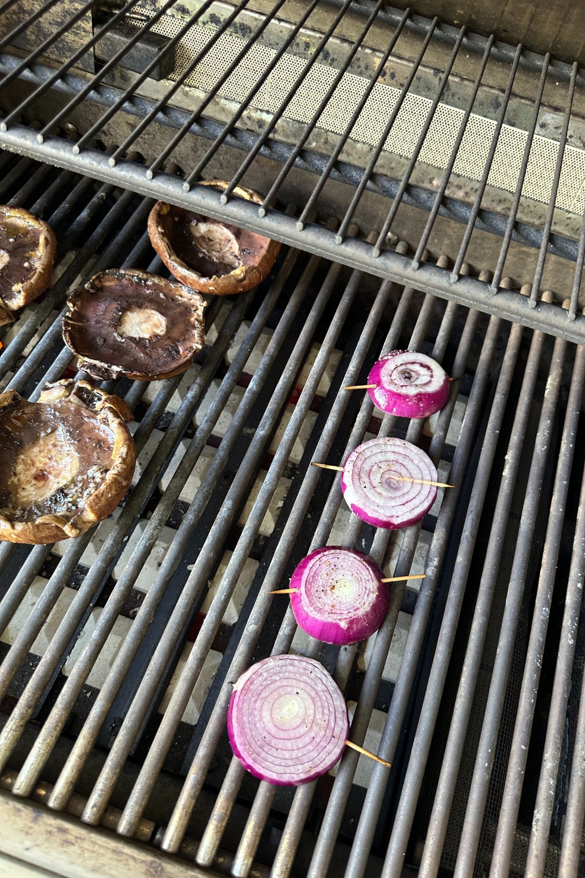 Grilled portobello mushrooms and onions cooking on a grill with char marks.