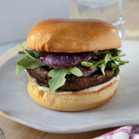 grilled portobello burger sandwiched between a bun with garlic chive aioli, lettuce, and red onion.