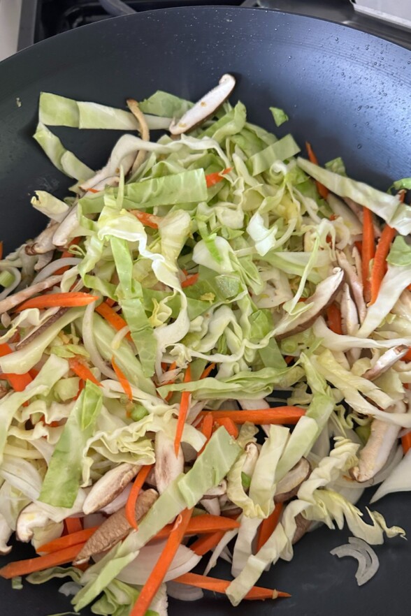 Sliced cabbage, carrots, mushrooms, and onions stir-frying in a large wok