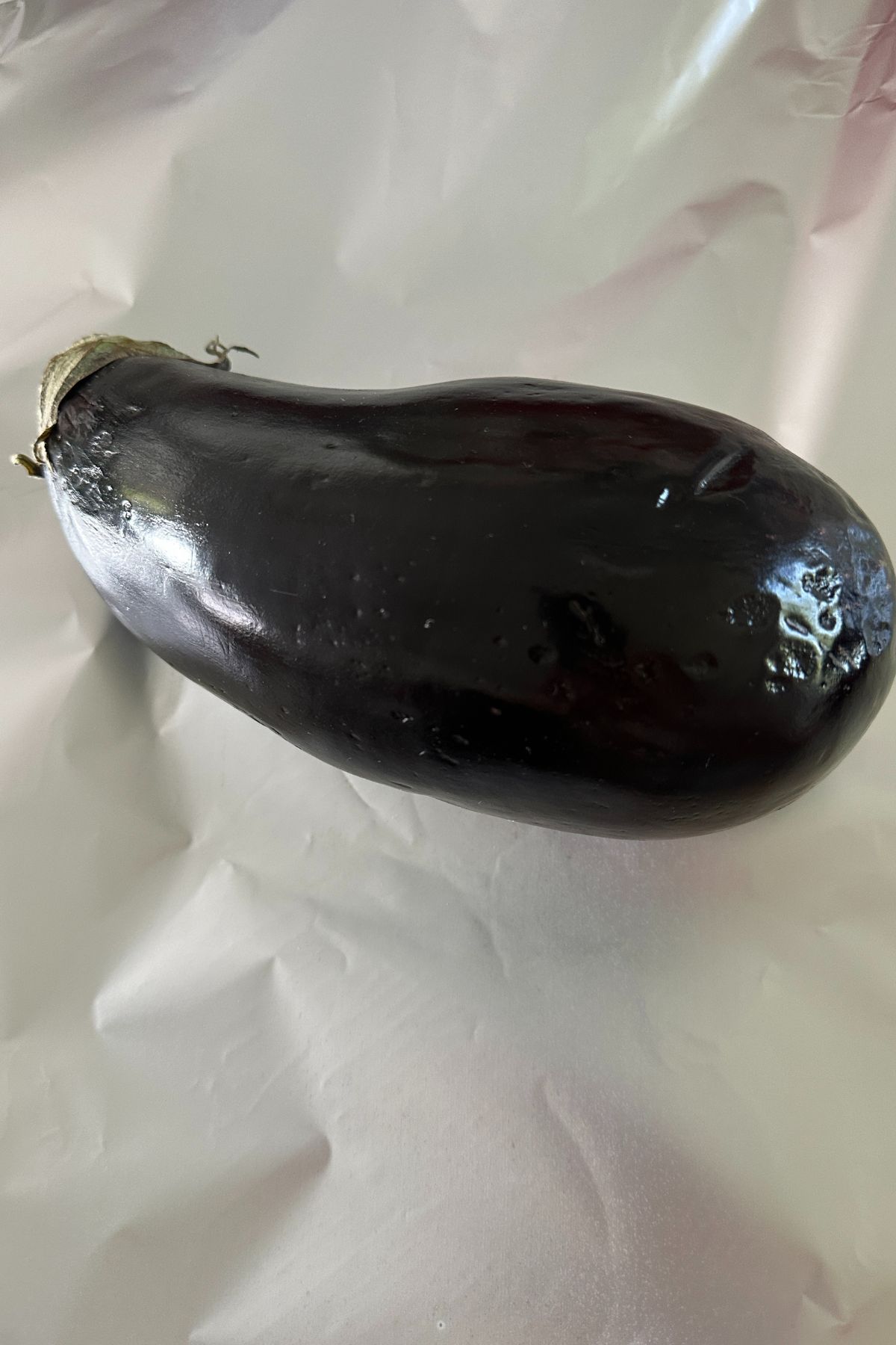 Whole eggplant wrapped in foil on a baking sheet before roasting