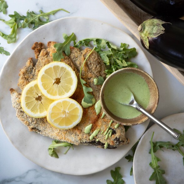 Crispy baked eggplant Milanese cutlets on a white plate served with basil-jalapeño sauce