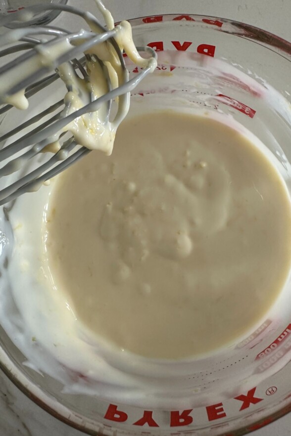 lemon filling in a white bowl with a whisk resting overhead ready to pour into the cooled crust