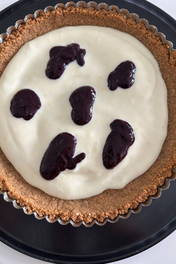 lemon filling in the tart crust with drops of blueberry swirl on top