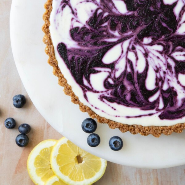 side view of a blueberry lemon tart swirled with blueberry next to a sliced lemon