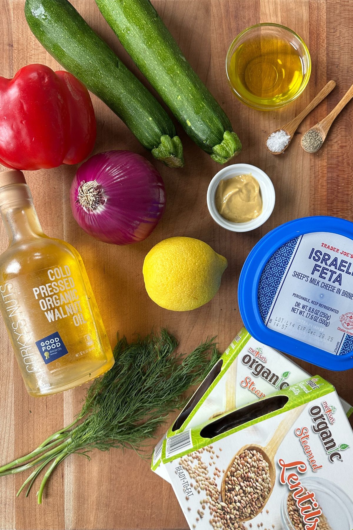 Ingredients for lemon dill dressing and optional grilled veggie salad displayed on a wooden cutting board, including fresh dill, lemon, Dijon mustard, olive oil, and walnut oil.