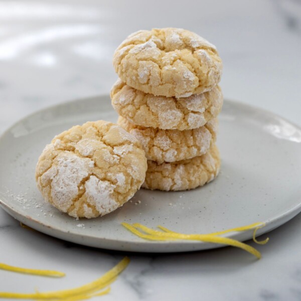 crackly lemon crinkle cookies stacked on a plate with powdered sugar tops