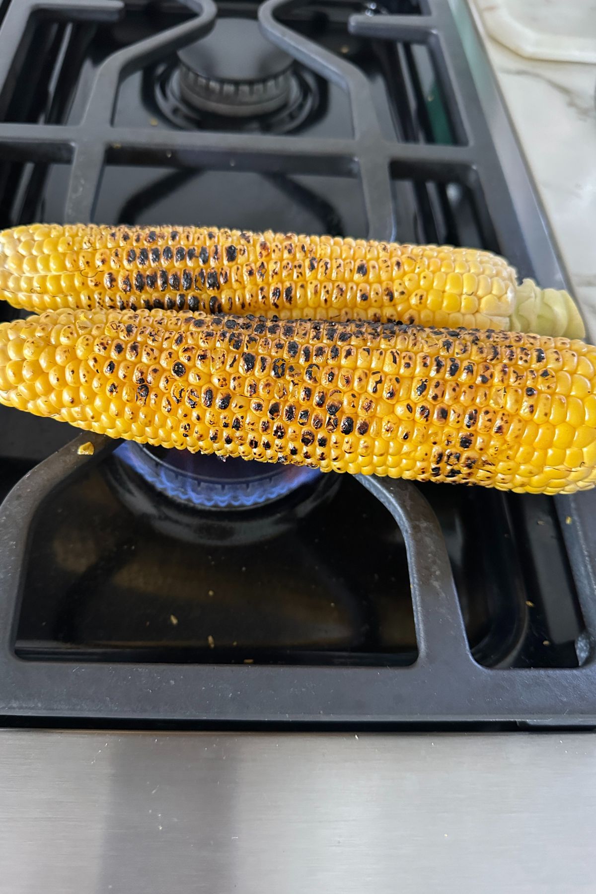 Two corn cobs laying on a black stove burner with visible char marks.