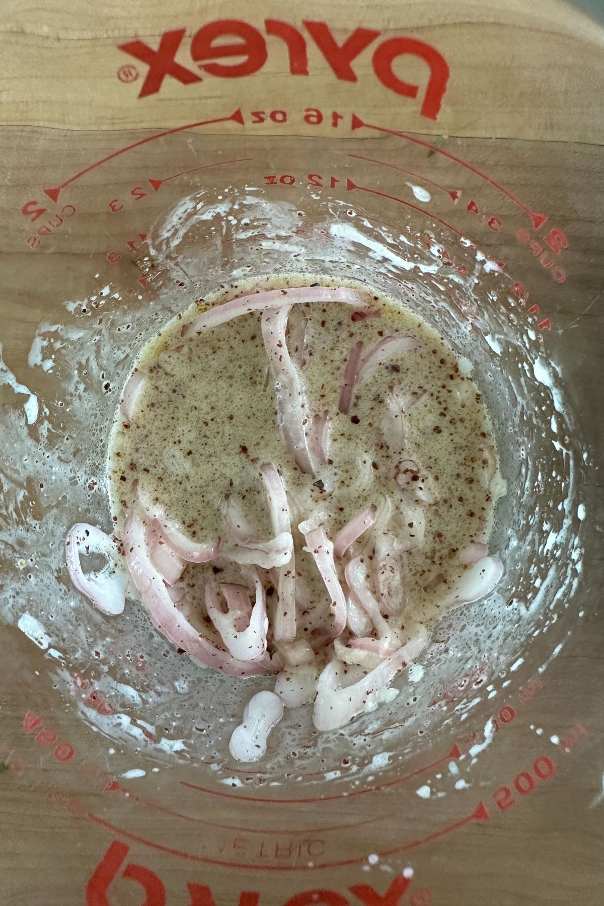 Summer corn salad dressing in a large glass measuring cup with visible shallots.