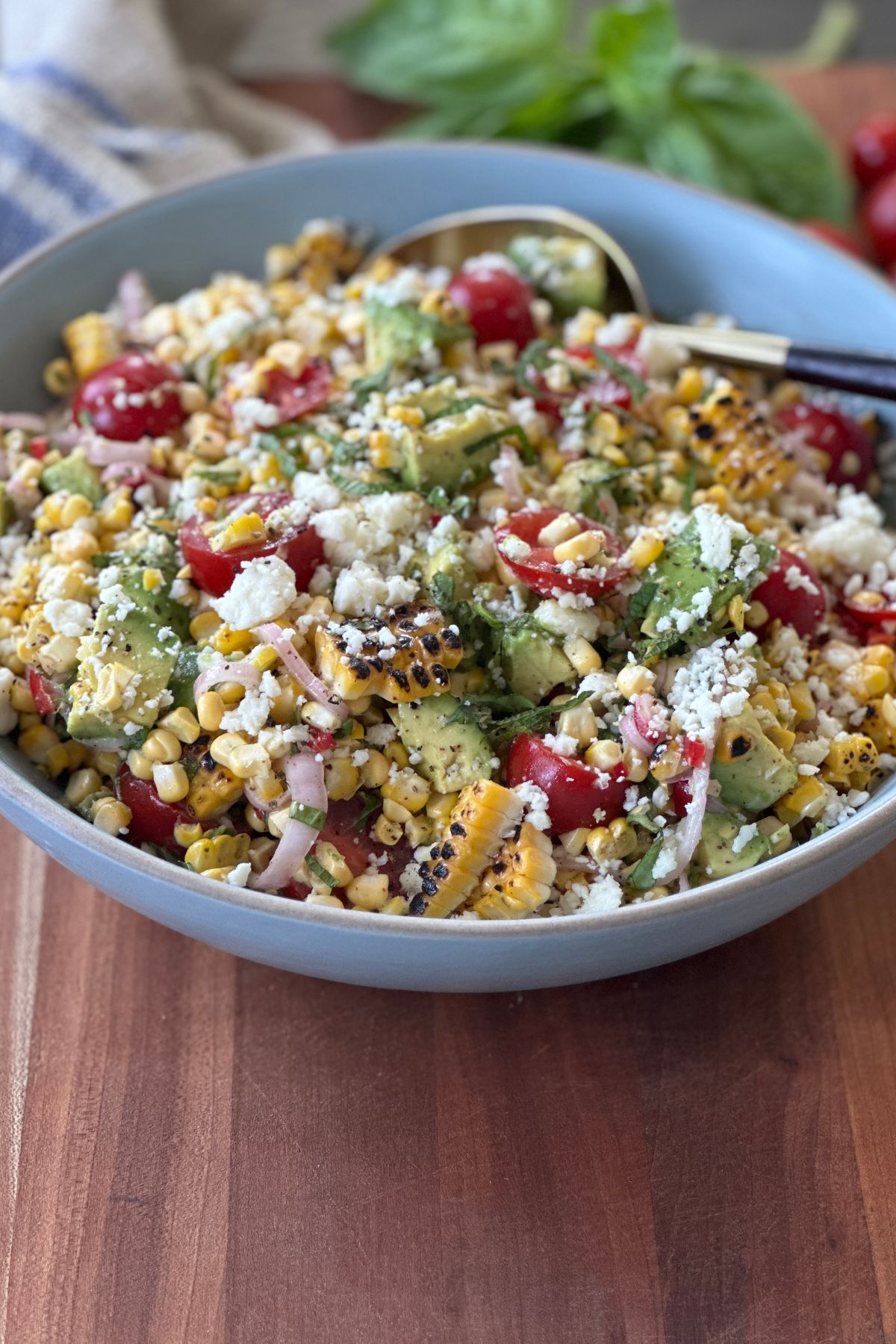 Fresh summer corn salad in a gray bowl with a spoon ready to eat. The bowl is on a wooden surface.