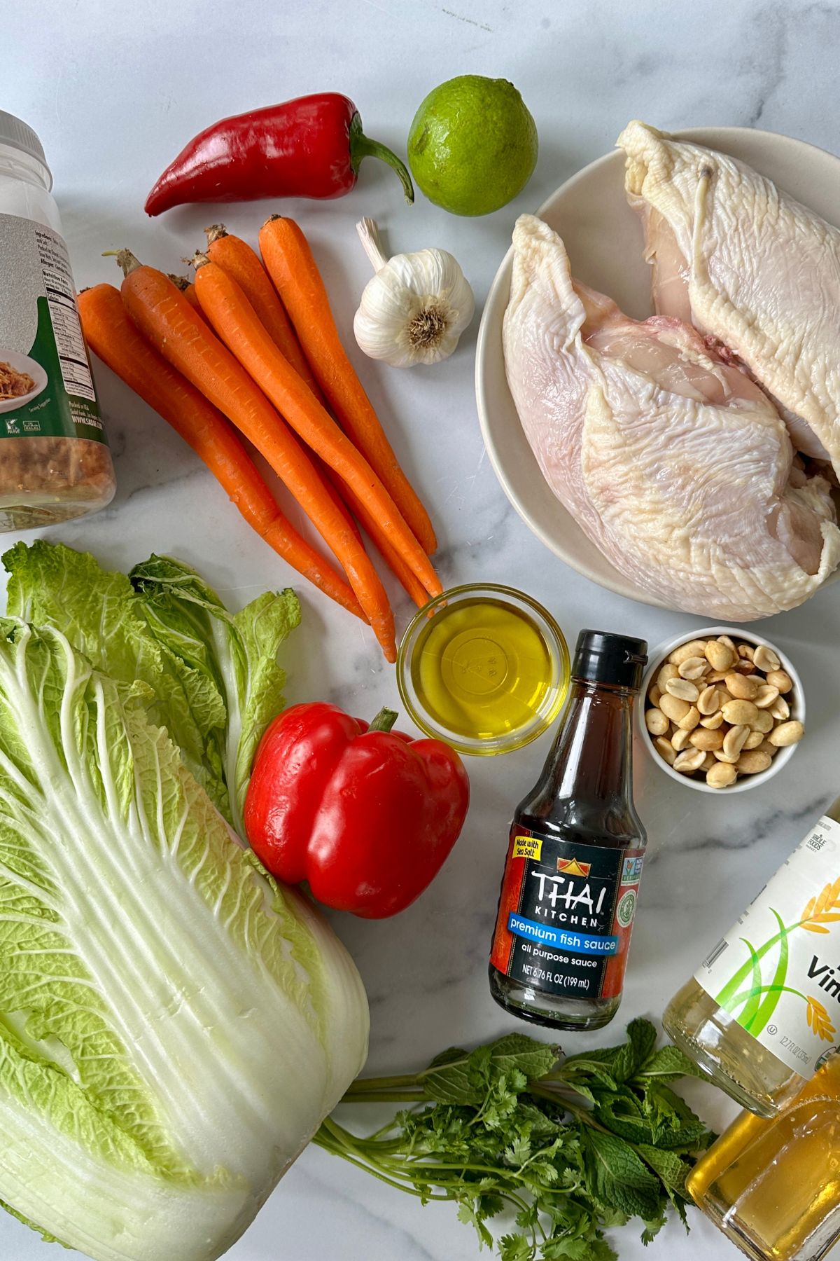 Ingredients for Vietnamese chicken salad including Napa cabbage, carrots, bell peppers, fresh herbs, poached chicken, and premium fish sauce.