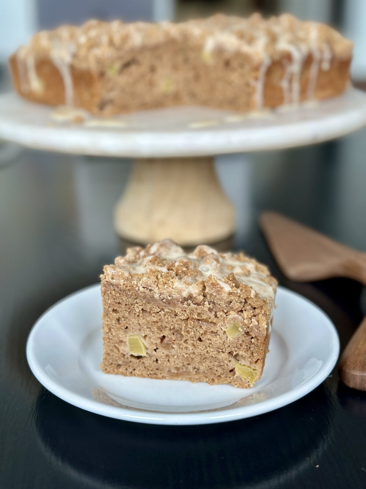 applesauce coffee cake on a white cake platter with a slice on a plate in front